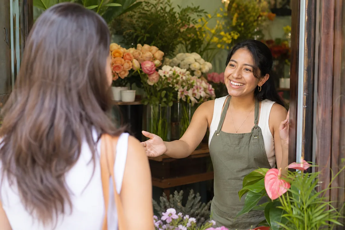 Florista recibiendo con una sonrisa a una clienta en la puerta de su tienda